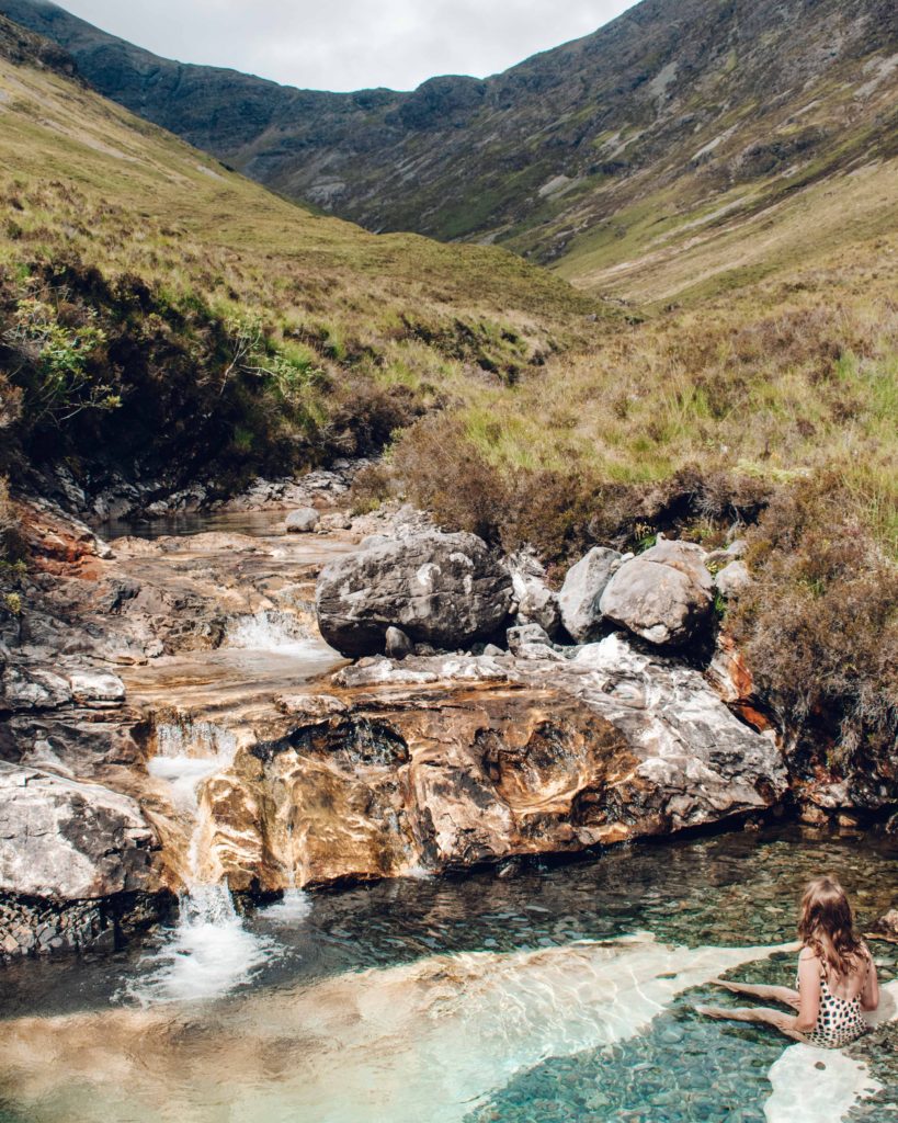 Woman sat in a natural water pool amongst Scottish mountains on the Isle of Skye 