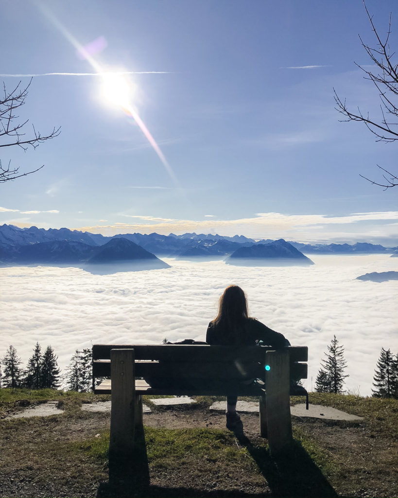 Woman sat on bench overlooking cloud inversion over Lake Lucerne