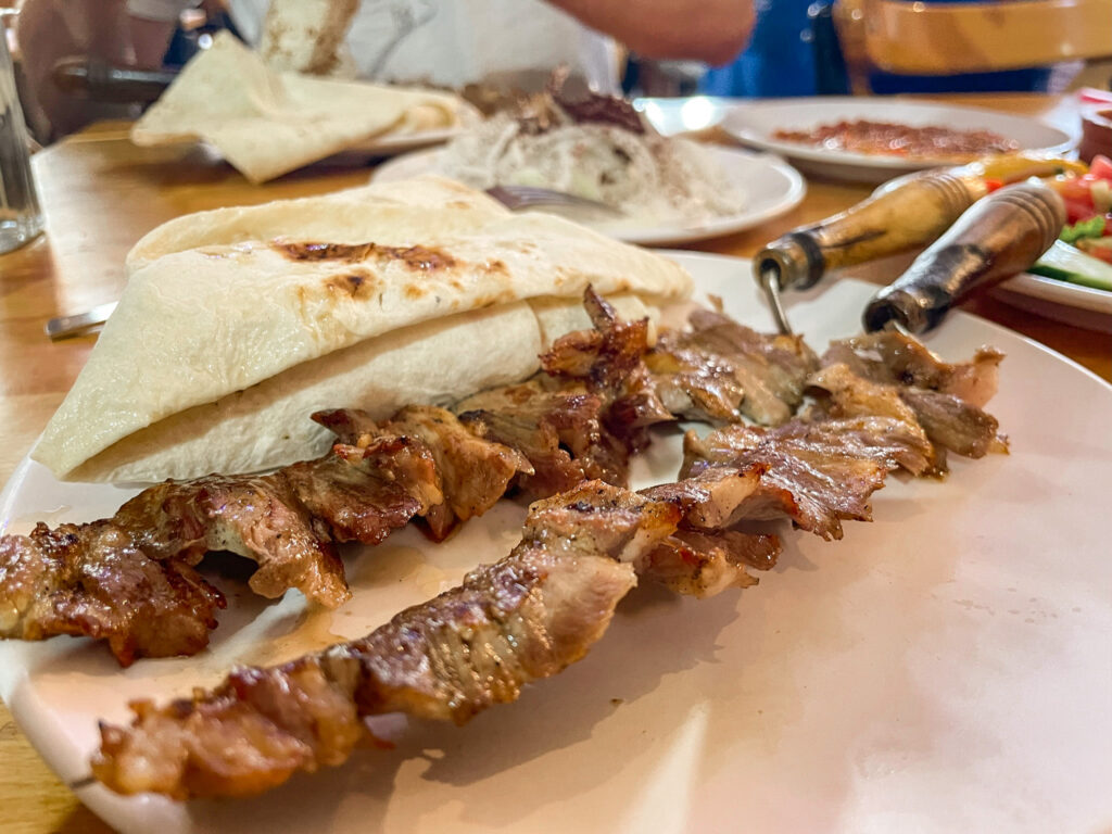 Cag kebab meat on wooden and metal skewers with thin flatbreads on a plate