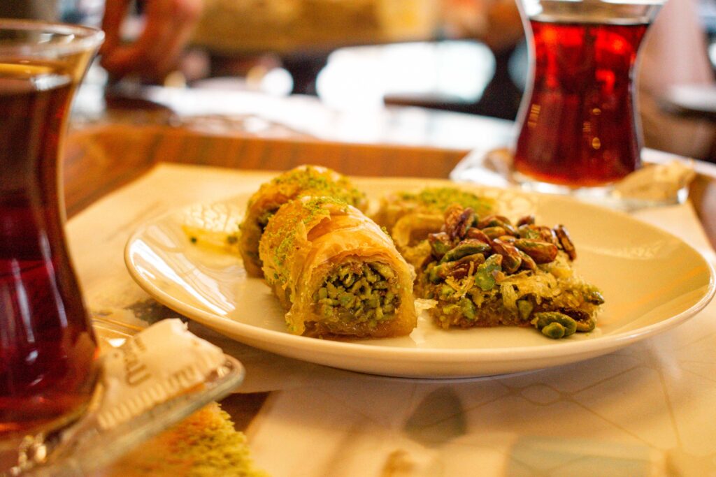 Selection of baklava on white plate surrounded by two glasses of Turkish cay (tea)