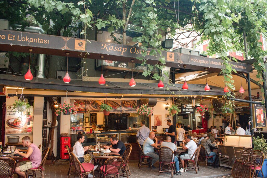 Customers sat at tables outside Kasap Osman under a green vine on a pergola, kebab restaurant in Istanbul