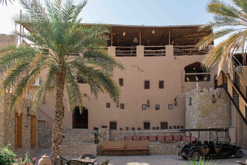 Cream fronted traditional Omani stone house, with small windows and timber covered roof terrace in Nizwa