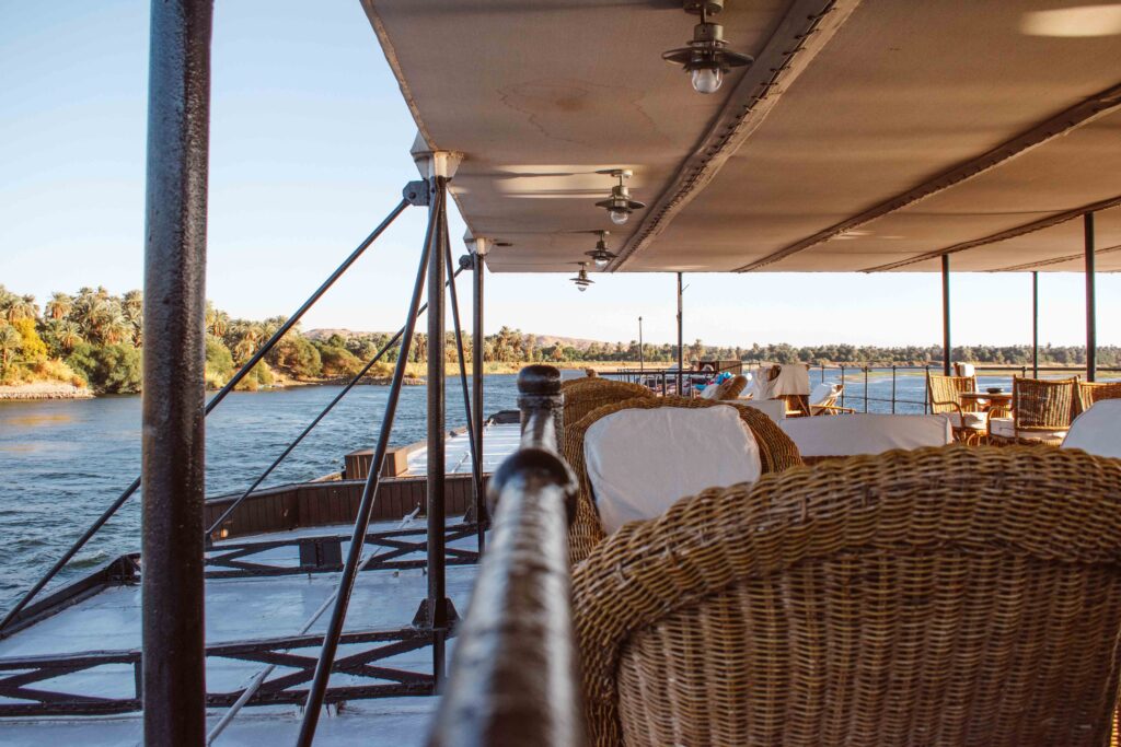 Wicker chairs with white pillows on the deck of a boat cruising the River Nile