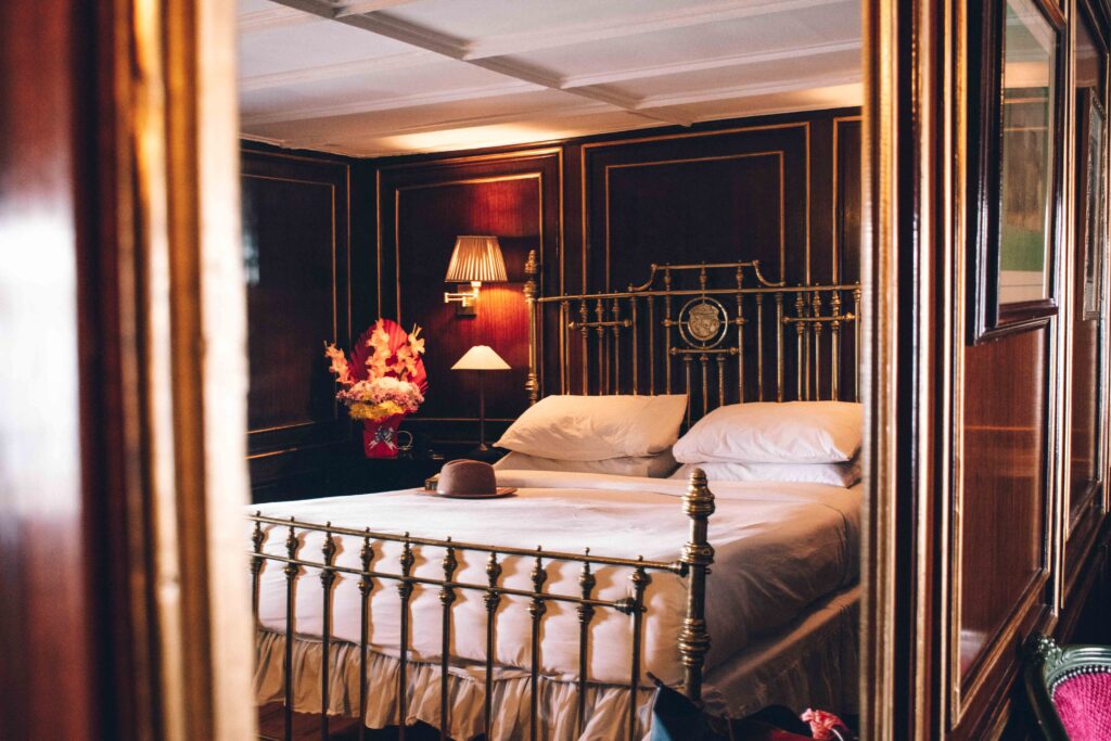 Reflection of a white sheeted bed in a gold framed mirror, in a wood panelled cabin aboard the Steam Ship Sudan