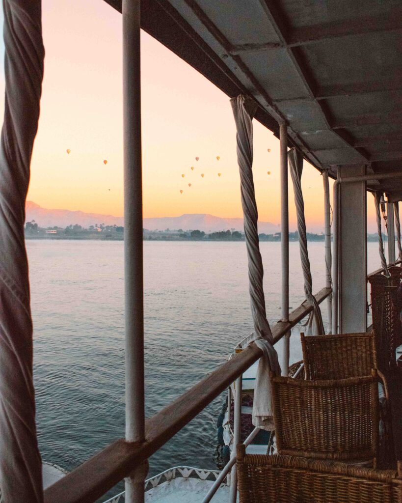 Hot air balloons in the distance taking off at sunrise seen between the slats of a boat deck on a Nile Cruise