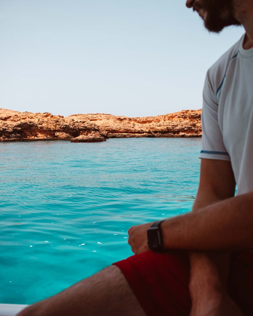 Man in white t-shirt looking out at turquoise water and rocky islands of Daymaniyat Islands