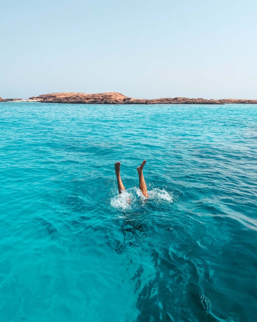 Man's feet sticking out of turquoise sea water after diving off a boat in the Daymaniyat Islands