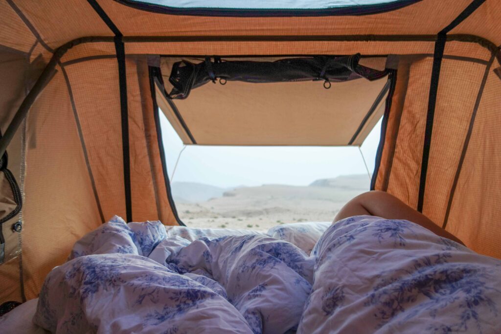 Man under a duvet looking at a distant view over the Salma Plateau, from inside a roof tent in Oman