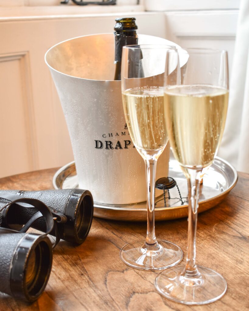 Two glasses of champagne in front of a silver ice bucket and black binoculars 