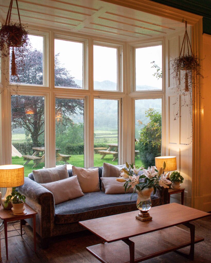 View over Lake District hills from large bay window filled with blue sofa and lamps