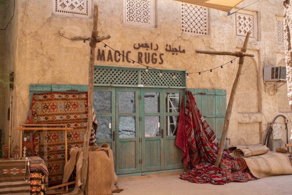 Woven red rugs hanging in front of antique looking shop front with weathered green doors in Dubai