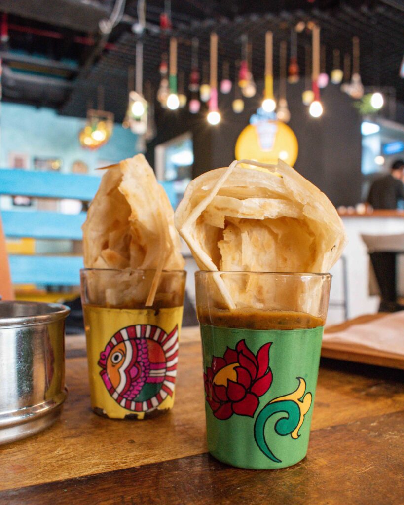 Brightly coloured glasses containing dal and flaky parathas at Bhukkad Cafe, Dubai