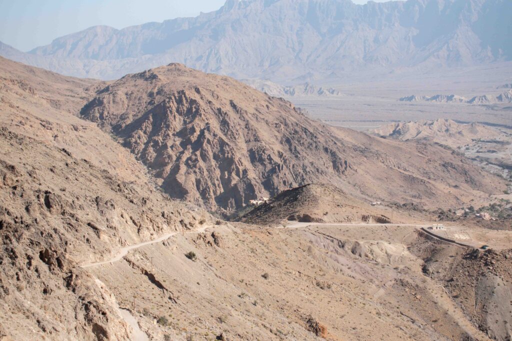 Panoramic view over dirt road on side of rocky hills up to Wakan Village, Oman