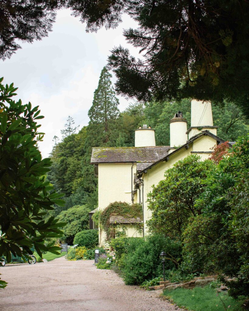 Yellow walls of The Lancrigg Hotel in the Lake District tucked amongst green trees and bushes