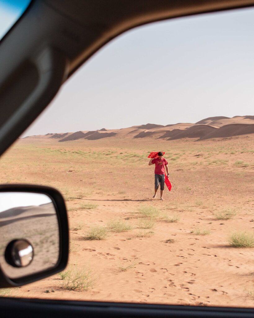 Man carrying sand tracks towards an open car window in the desert, Wahiba Sands, Oman