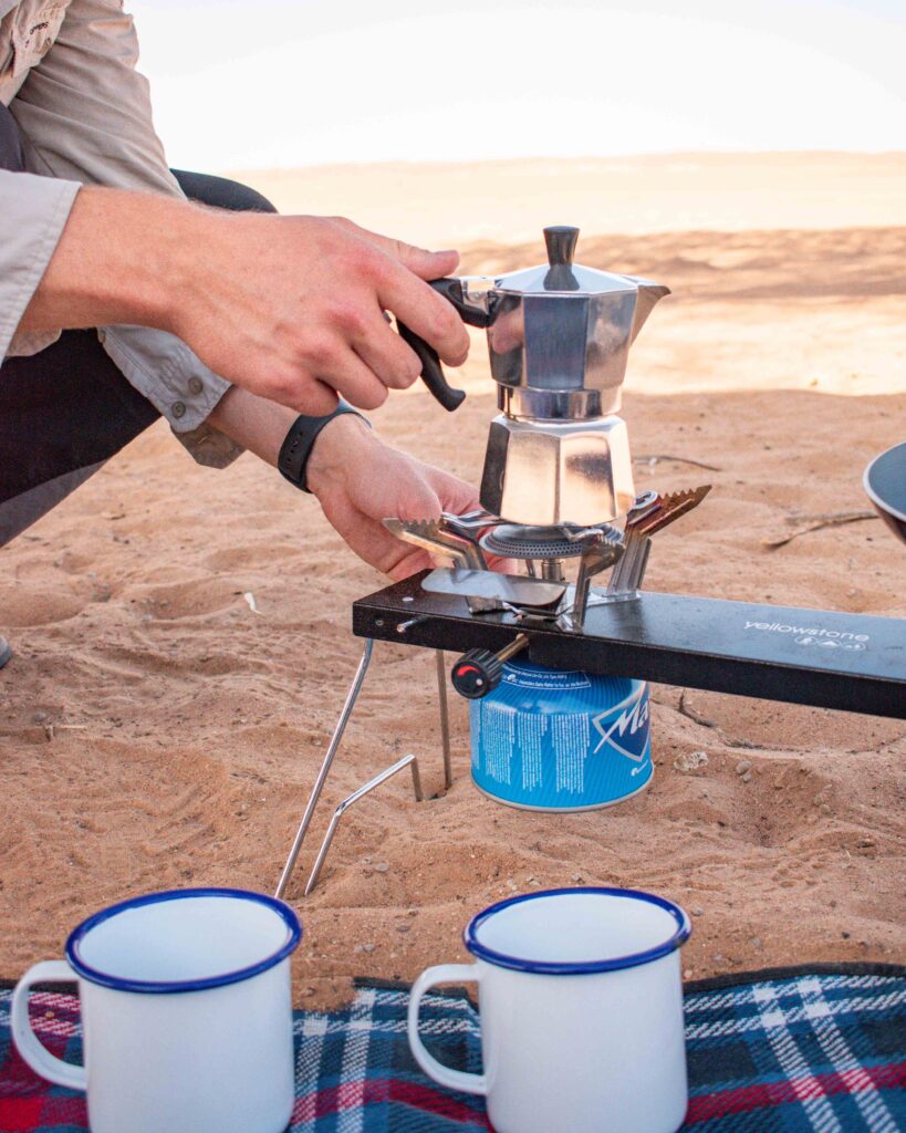 Man making coffee in a moka pot on camping stove in sand dunes, Oman