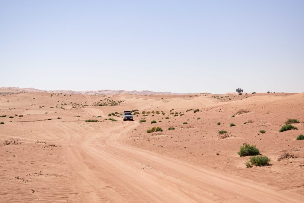 White car driving on off road track through desert of Wahiba Sands, Oman