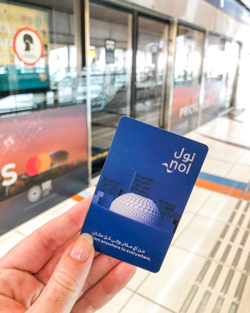 Woman's hand holding a blue "Nol" travel card on the Dubai metro system