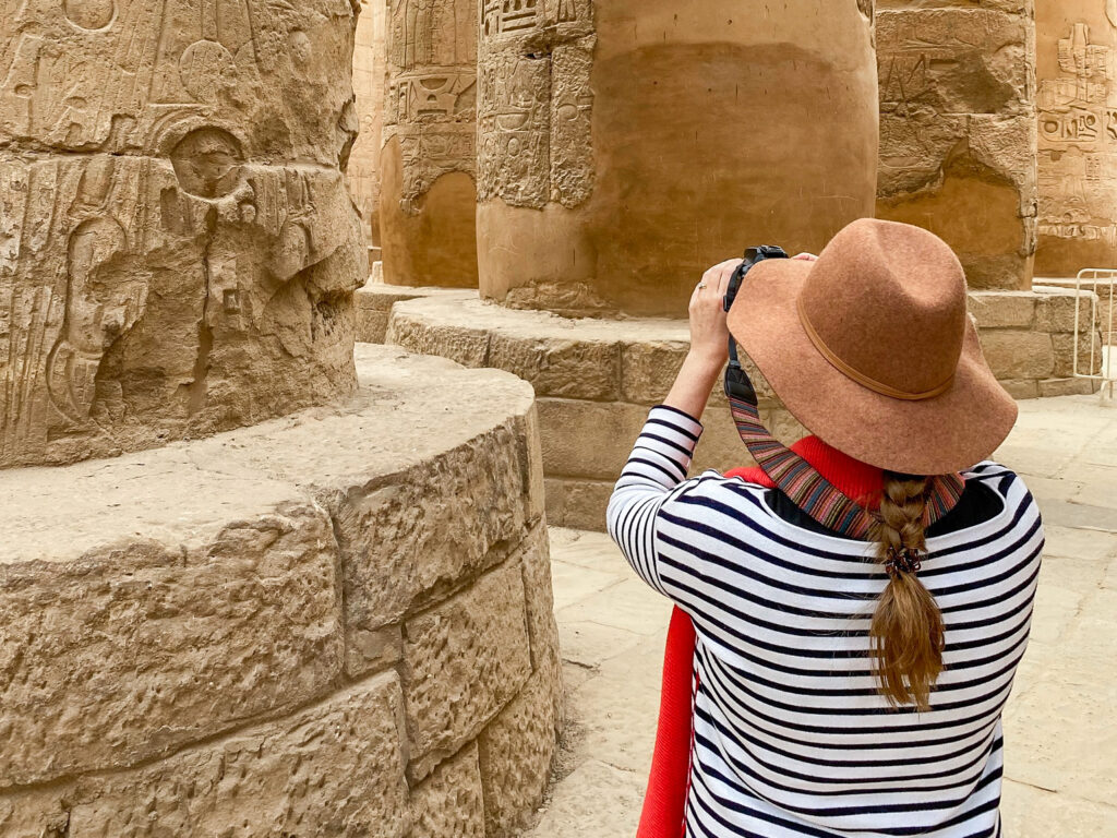Woman in brown hat and striped jumper photographing the Great Hypostyle Hall in Karnak Temple, Egypt