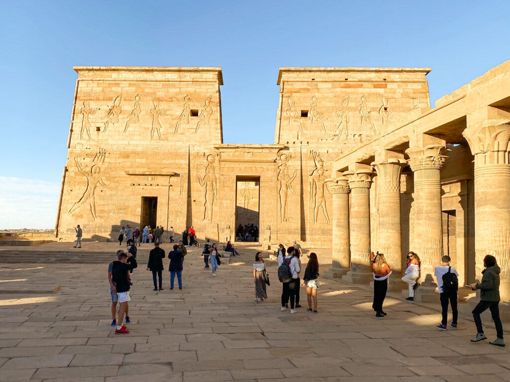 People in front of the carved stone front of Temple of Isis at Philae, Egypt, in glowing afternoon sunshine