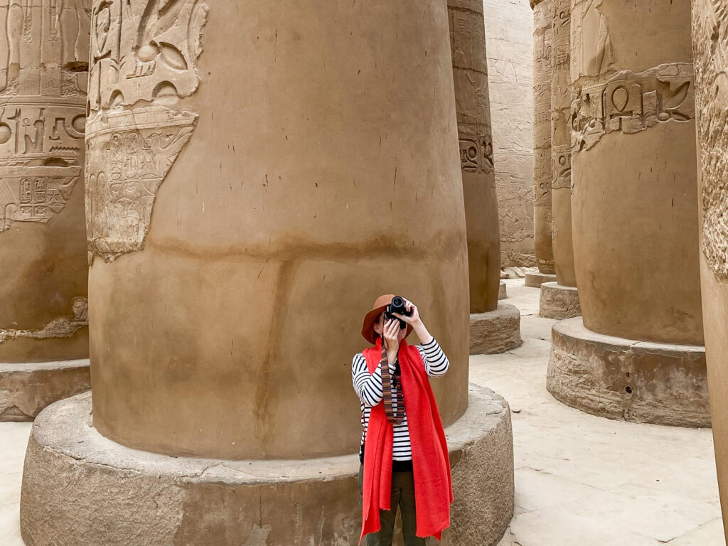 Woman in bright red scarf and brown hat photographing Karnak Temple, Egypt