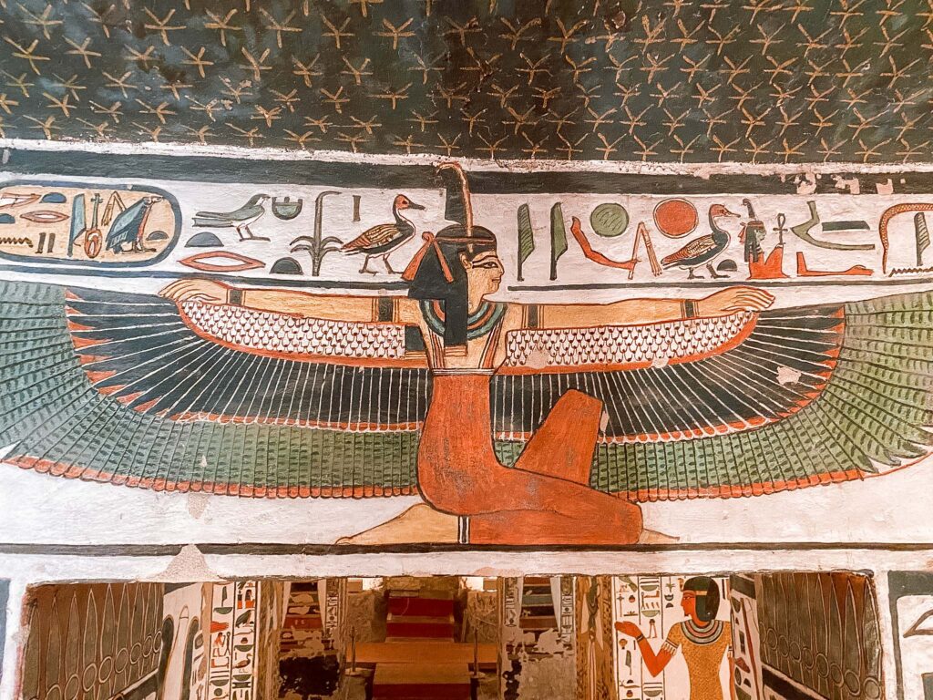 Intricately painted colourful winged woman and hieroglyphs and figures on wall in the tomb of Nefertari