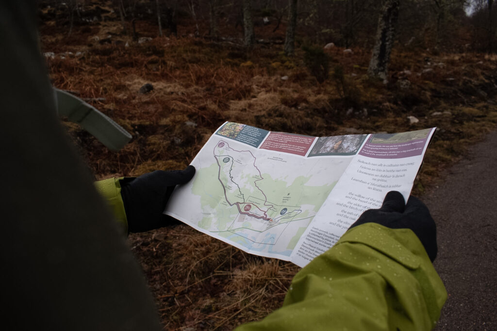 Close up of a paper leaflet map of Dundreggan Rewilding Centre held by a man wearing black gloves and a wet, green waterproof jacked. 