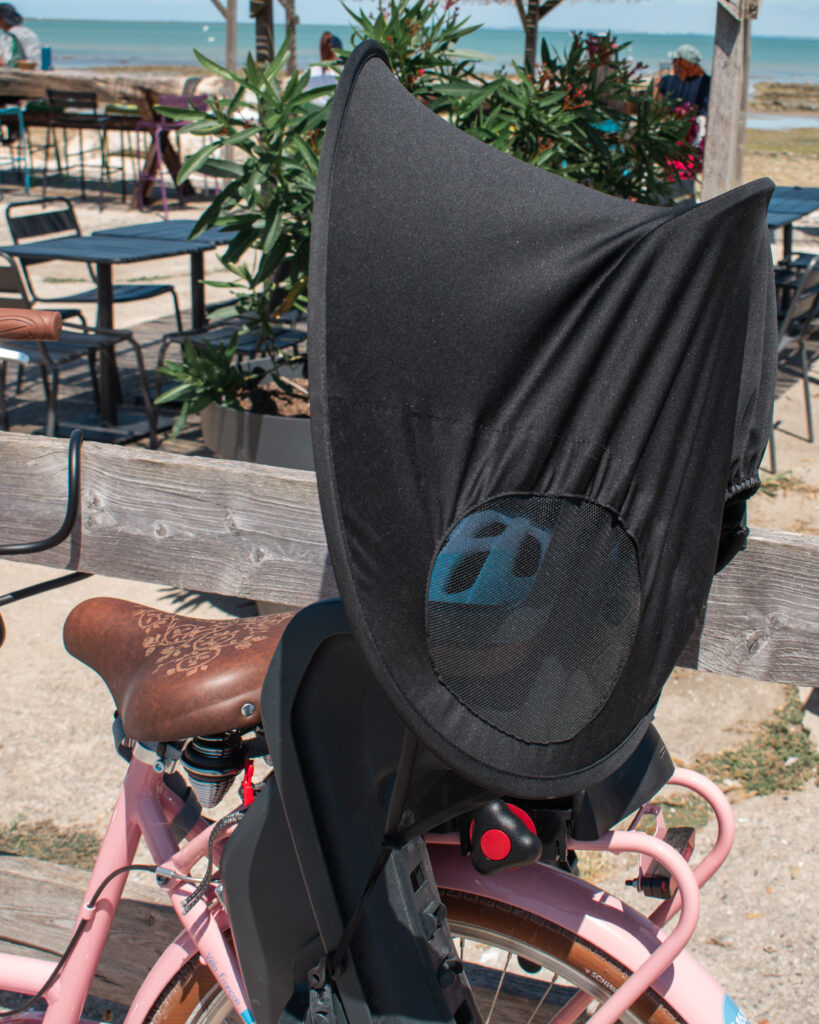 Close up photo of a black pram sun shade, rigged up as a sun canopy for a child's bike seat.
